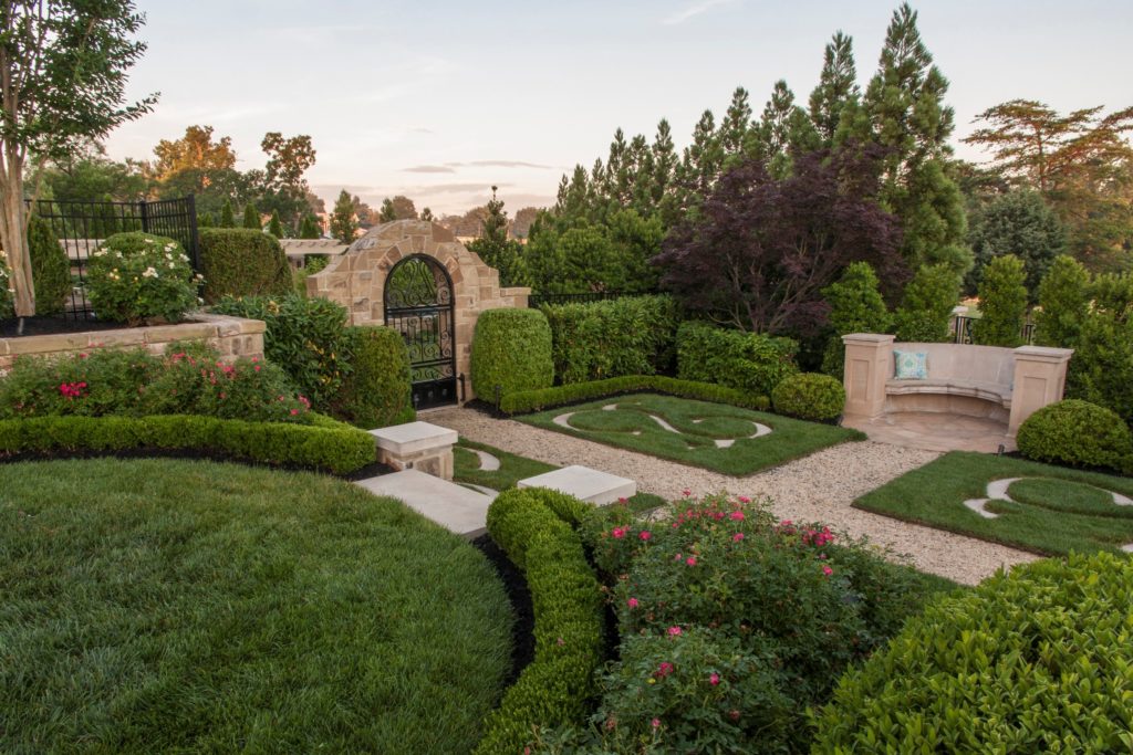 Large landscaped garden with brick pathways and black gate with stone surround.