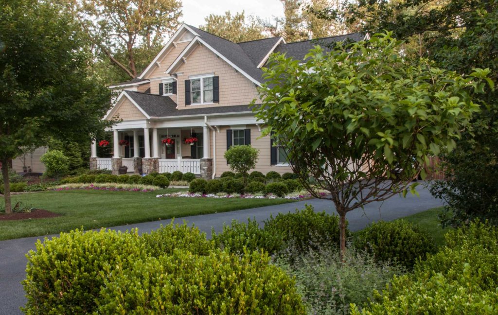 Custom paved driveway design in McLean, Virginia, next to a large beige home with landscaping and a covered front porch.