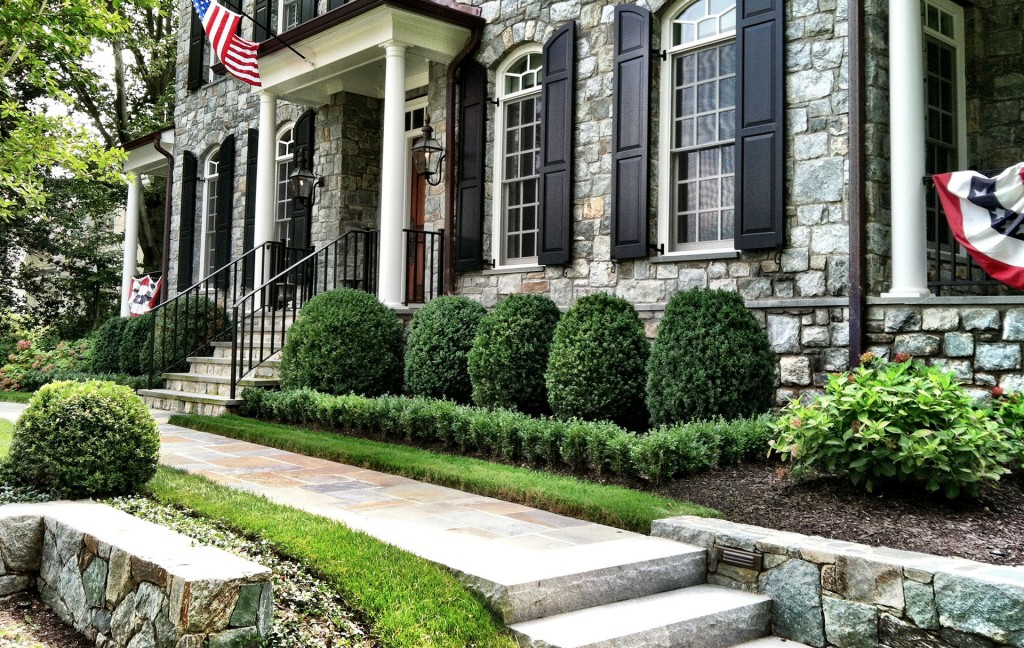 custom outdoor front entry walkway design in McLean, Virginia, leading up to large colonial-style stone house with landscaped bushes in front.