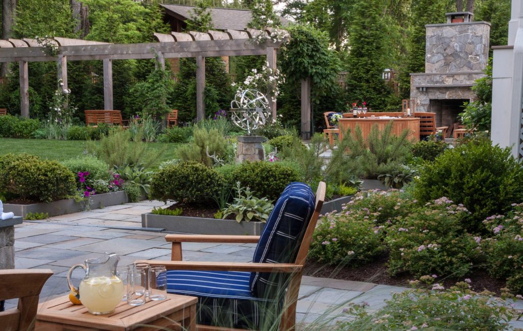 Residential custom-built backyard entertainment space & outdoor patio in McLean, Virginia. Landscaped bushes and flowers surrounding, with trees in background.