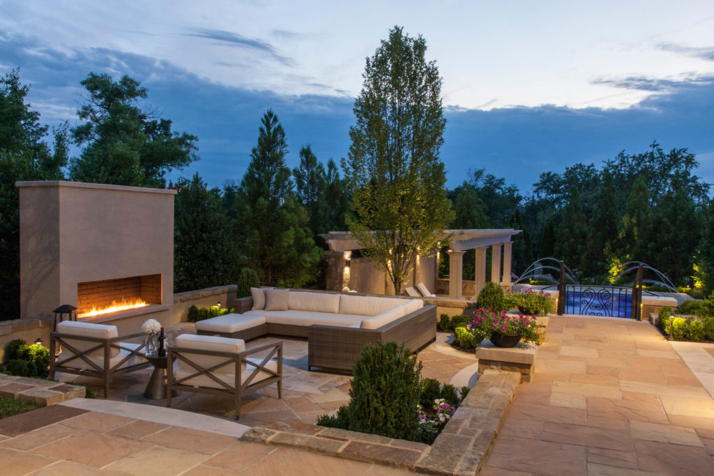 Landscape maintenance & design in Maryland, patio design, patio landscaping. Sunken stone seating area and outdoor fireplace with decorative shrubs around.