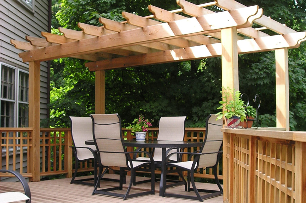 Pergola design over a new deck installation with set of table and four chairs. Trees in background.