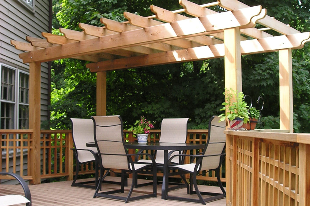 Pergola design over a new deck installation with a table and four chairs. Trees in background.