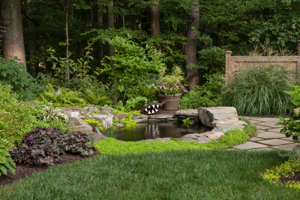 Water feature in wooded backyard with flowers and stones around it