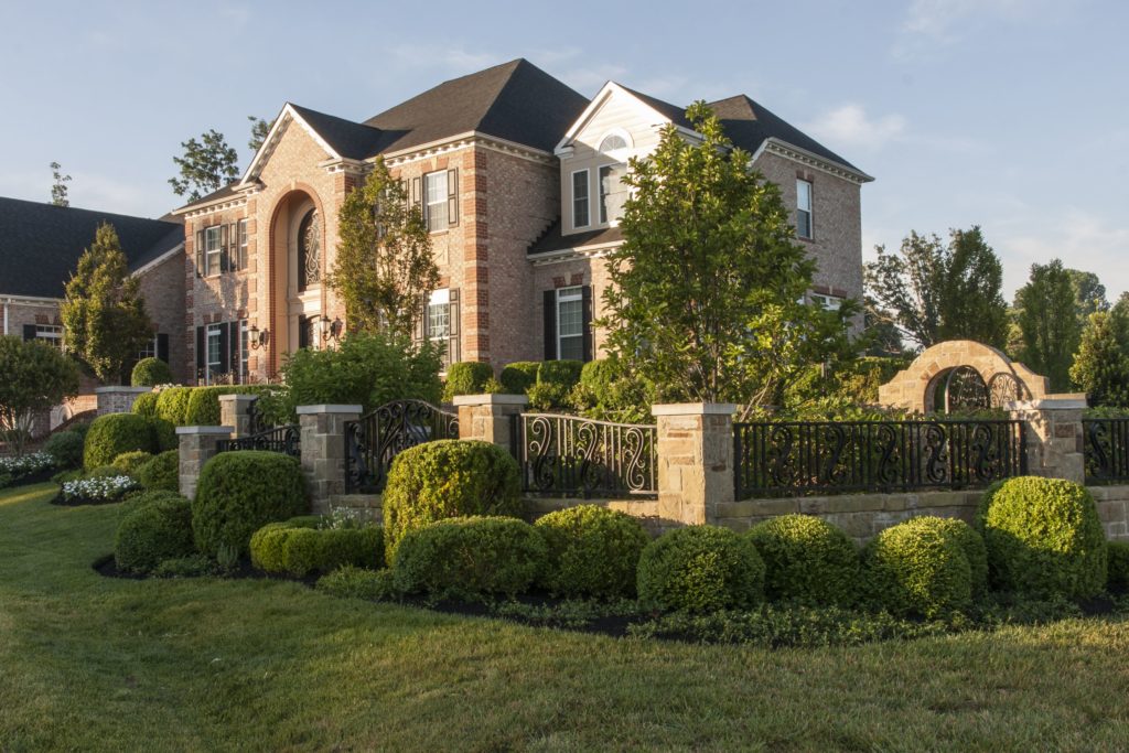 A spacious brick home with a stone fence and hedges, complemented by perfectly trimmed trees.