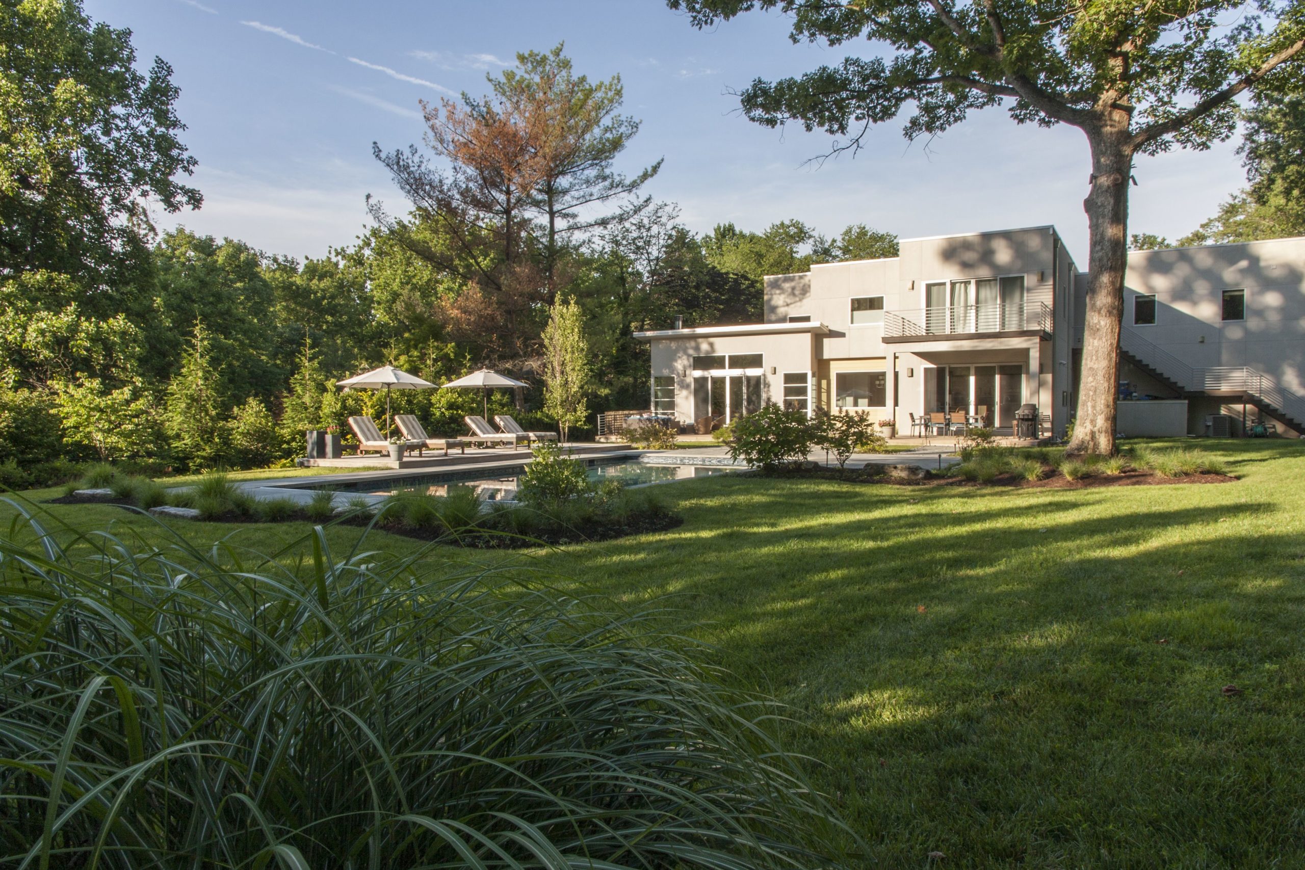 An image of a modern residence featuring a vast lawn, trees, and a recently renovated landscape.