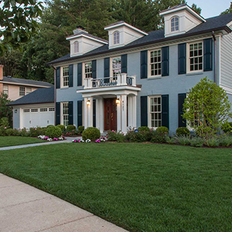 A serene blue house with white shutters complemented by a vibrant green grassy landscape.