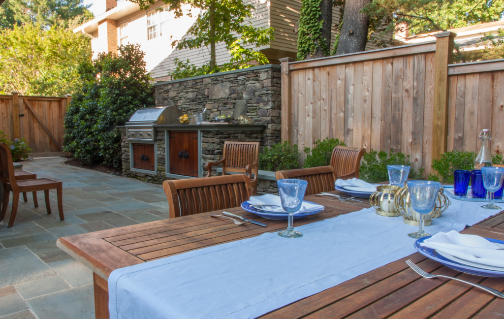 Wooden table outside with a view of outdoor grill set into stone wall.