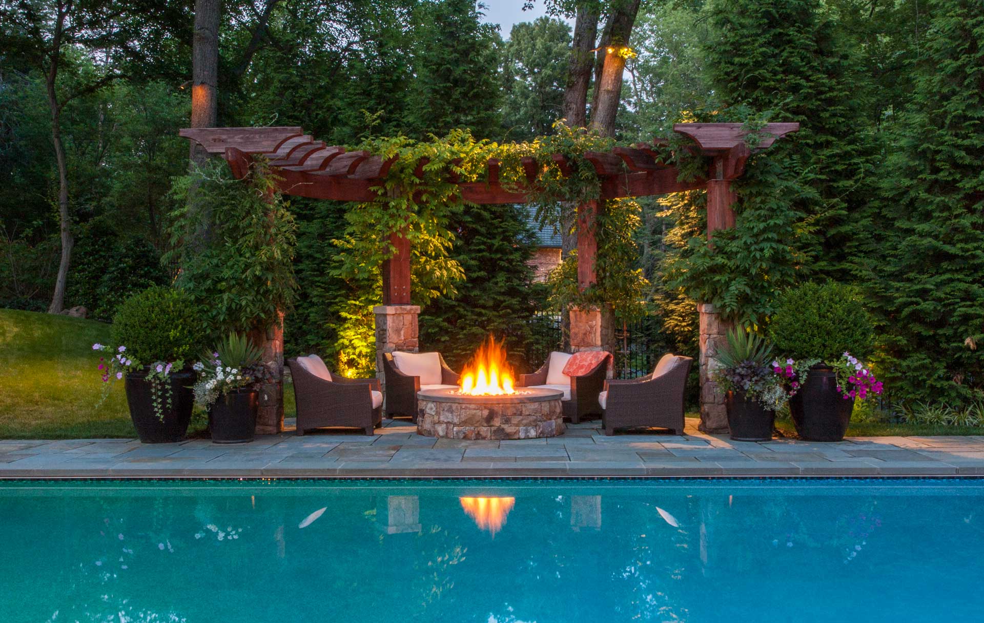 In a home's backyard, a fire pit is nestled amidst potted flowers, creating a tranquil and shaded setting.