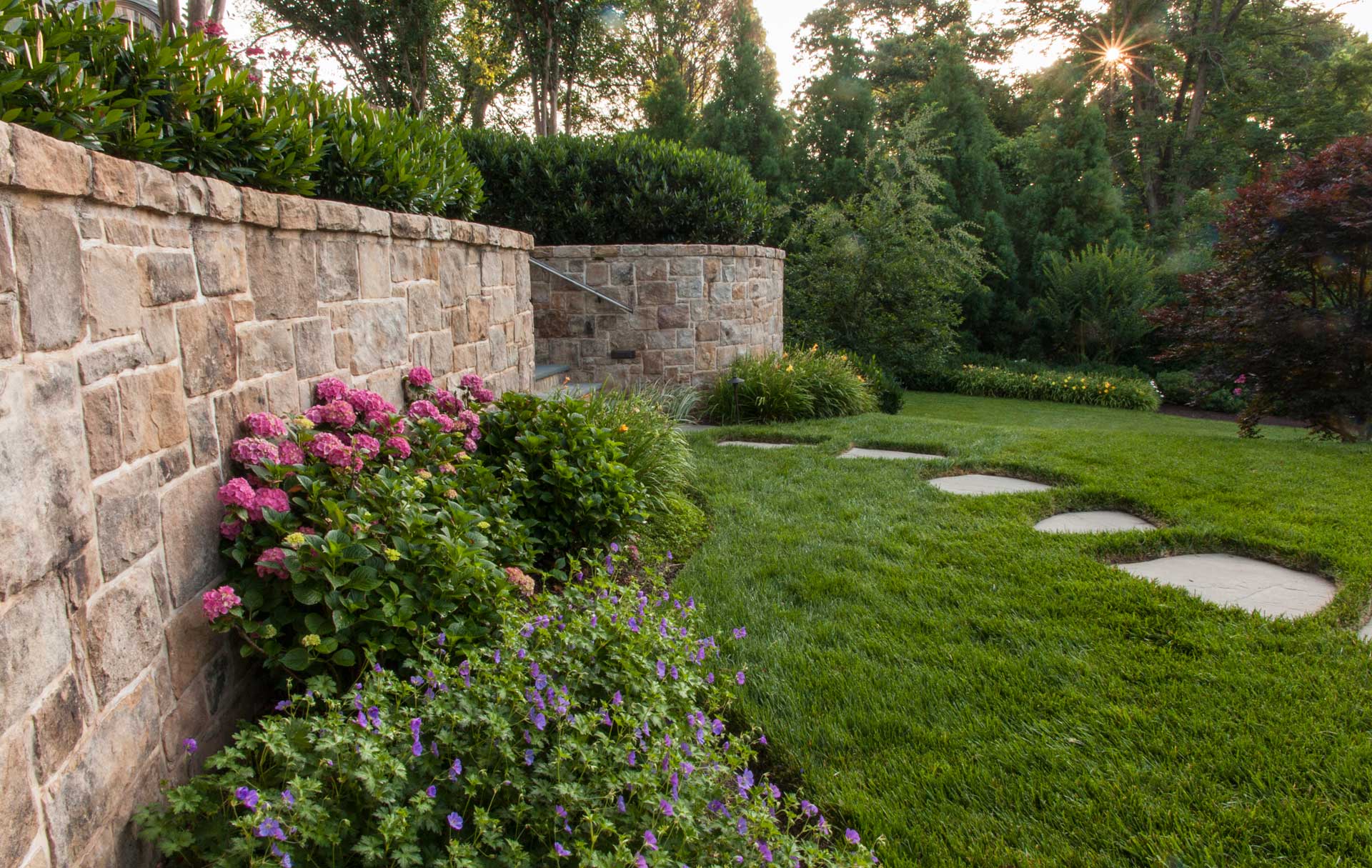 Stone wall and steps and flower beds in a backyard, creating a serene and charming outdoor space.
