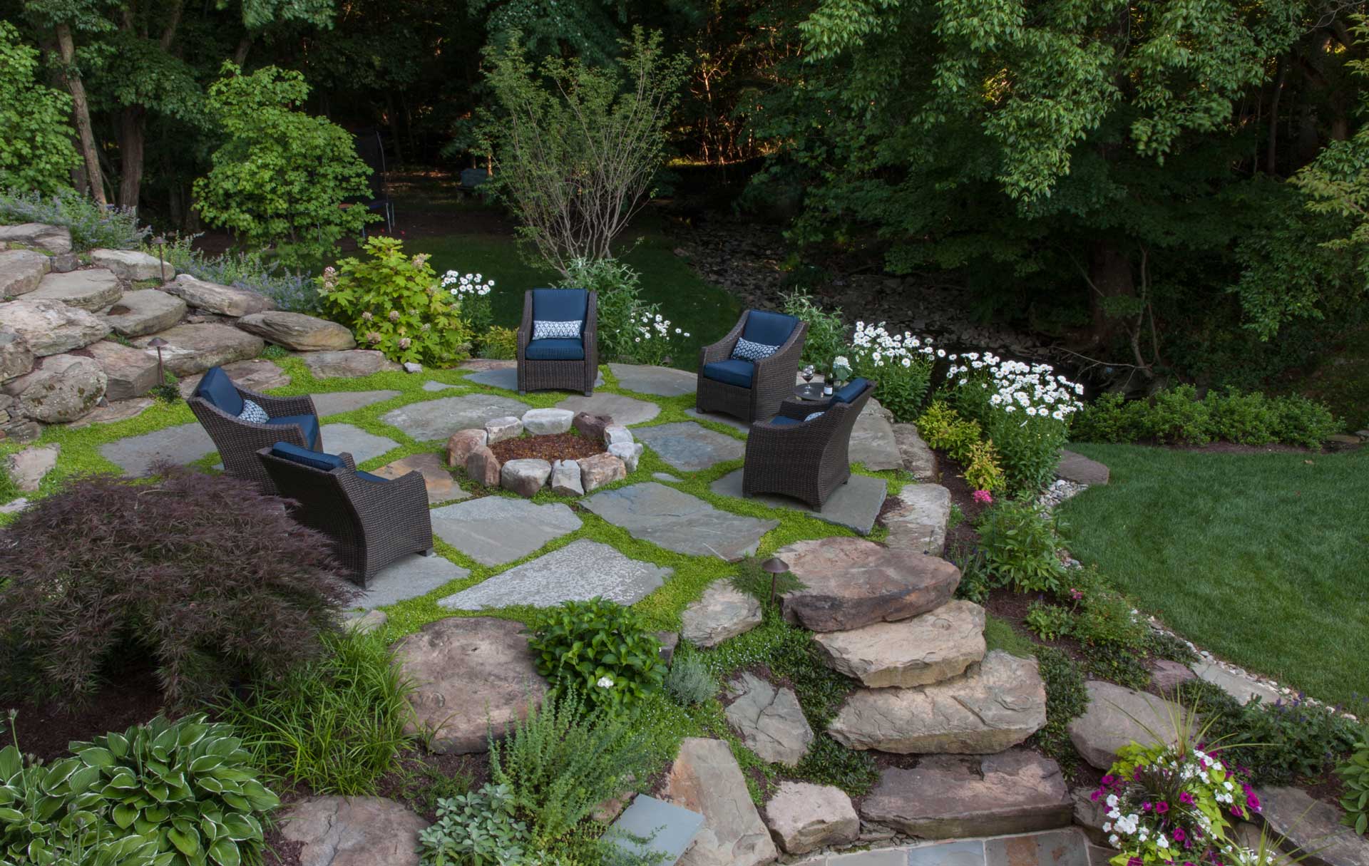 A backyard adorned with stone steps, a fire pit, and seating area, providing a tranquil setting for outdoor enjoyment.