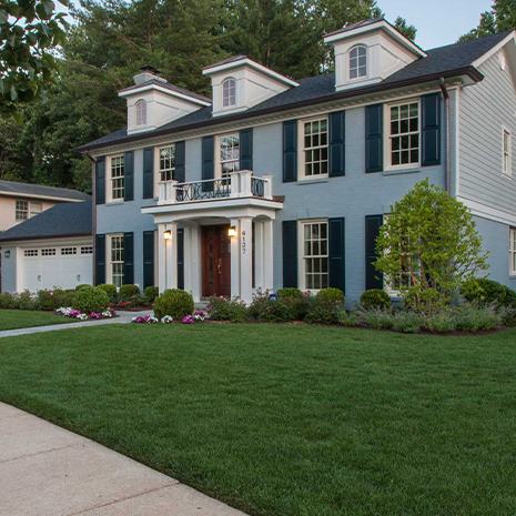 A serene blue house with white shutters complemented by a vibrant green grassy landscape.