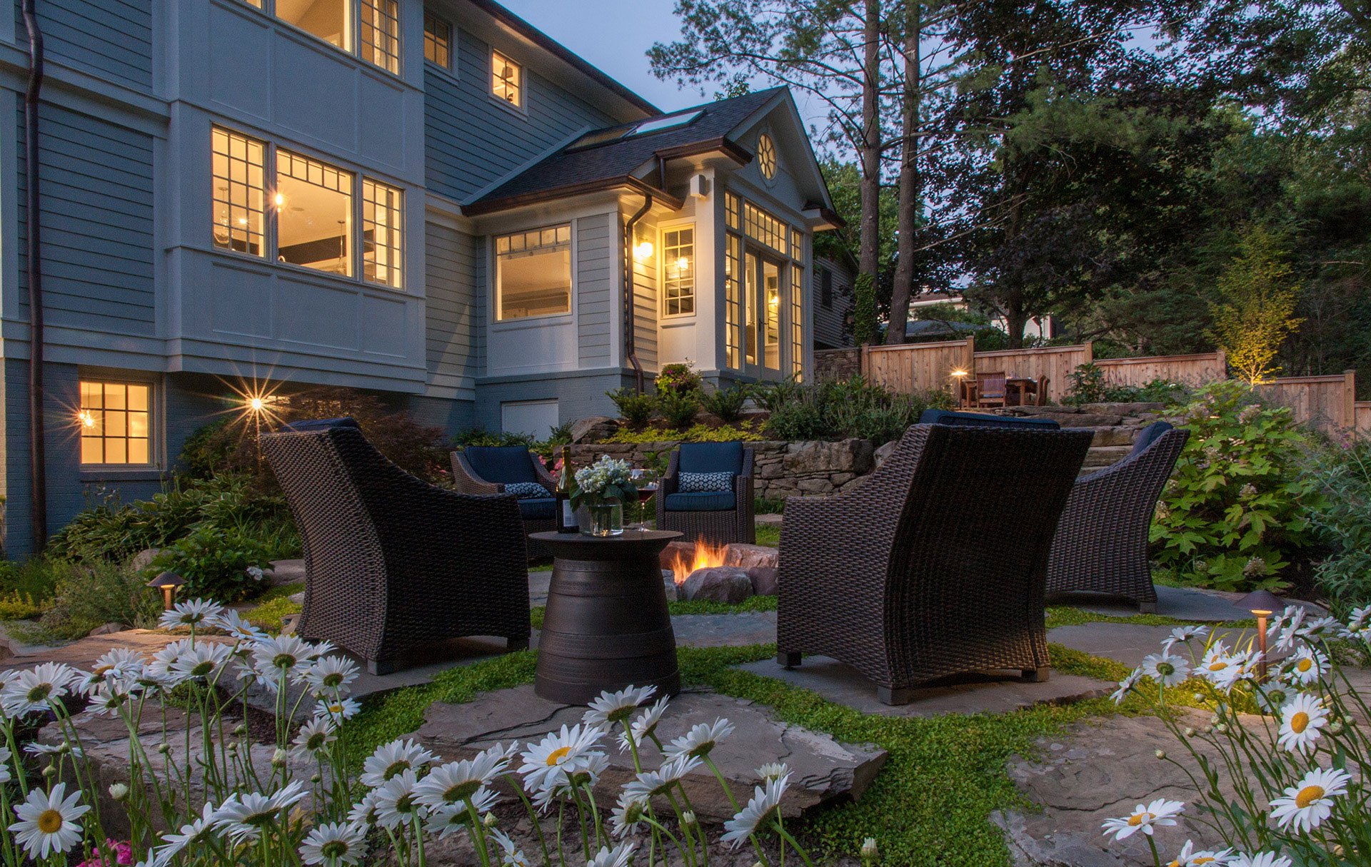 A modern swimming pool with a sleek design, surrounded by lush greenery, lounge chairs, and a firepit.