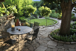 Metal table surrounded by metal chairs in a landscaped yard with trees and stone paths