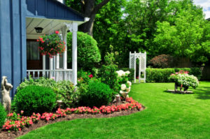 White porch on a black house, surrounded by flowers, shrubs, and green grass
