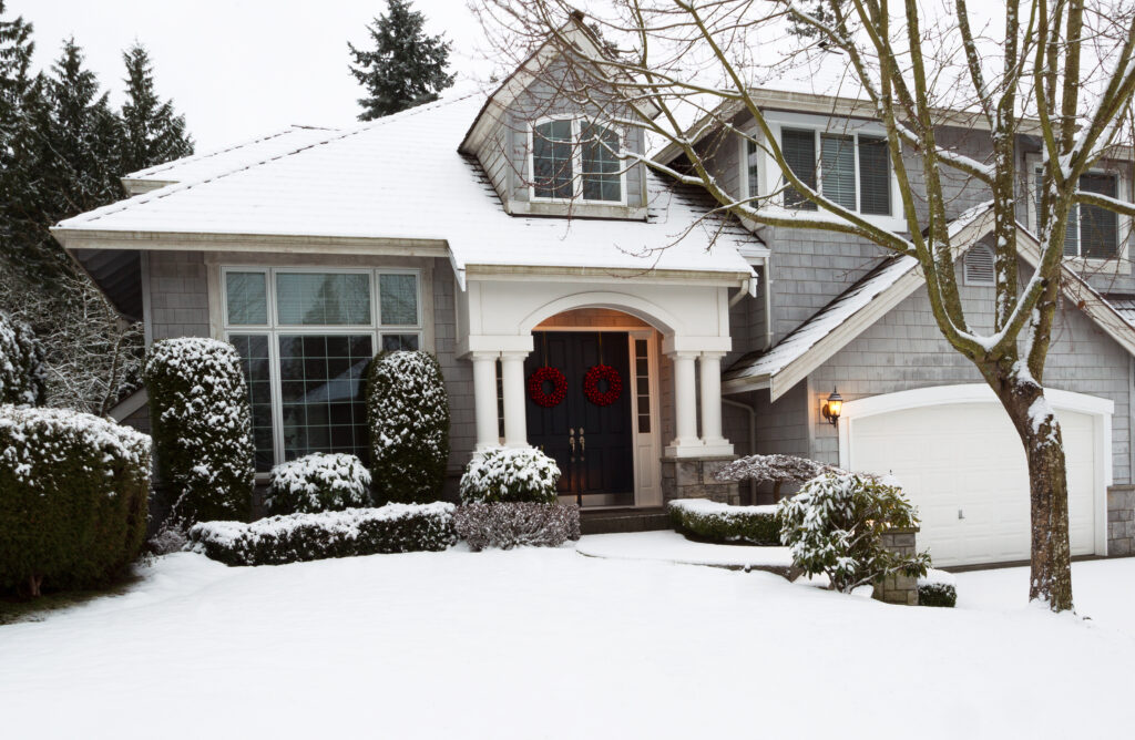 Front yard of home during the holidays with fresh snow fallen on green shrubs and on house